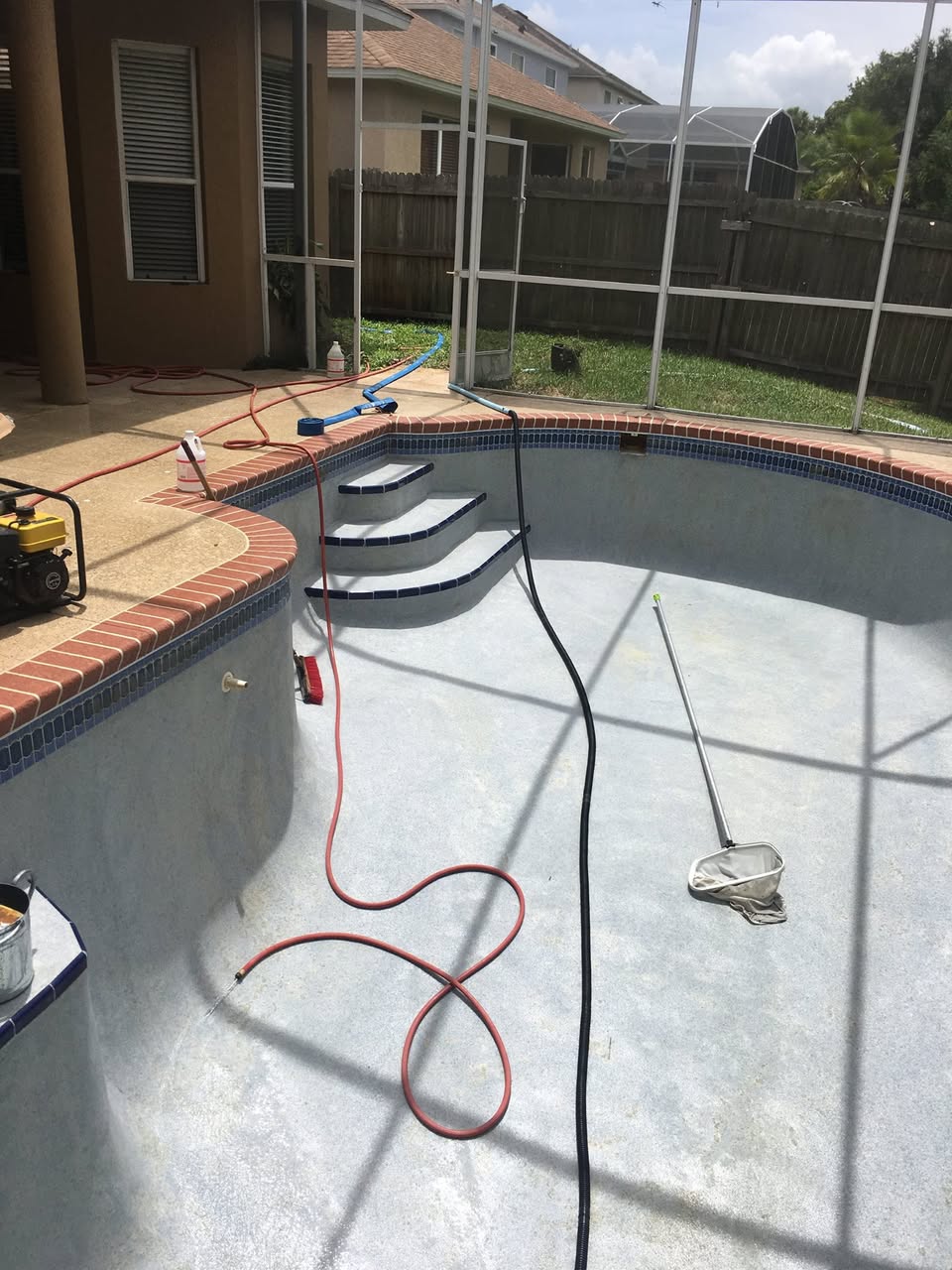 Drained Orlando pool with stained plaster mid-recovery, brush and net staged on steps